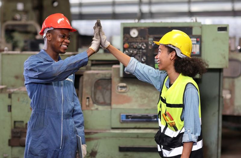 Two young workshop apprentices in safety helmets sharing a high five