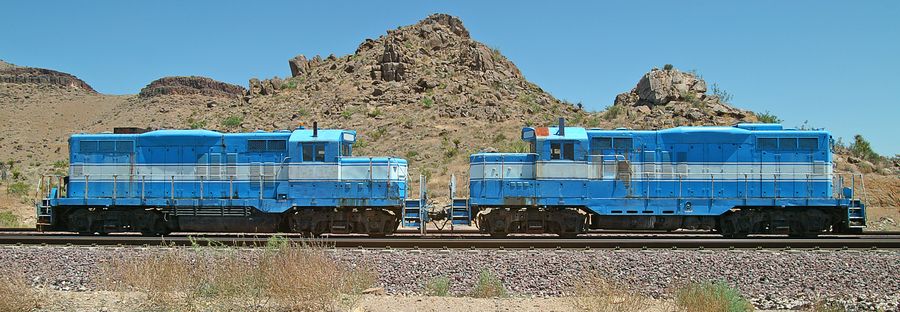Two blue diesel locomotives standing on a line below a rocky hill