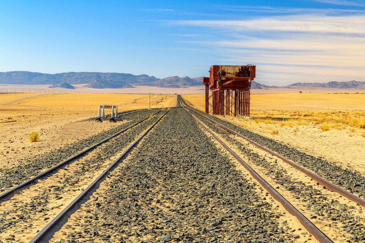 A desert railway line in southern Namibia running towards distant mountains, with an old water tower beside the track