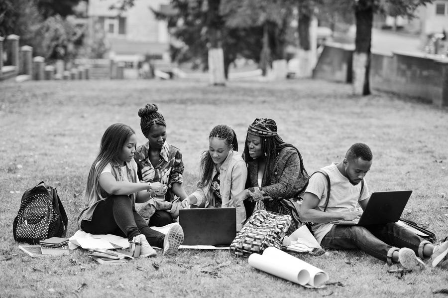 A group of African students gathered on grass with laptops, collaborating on work.