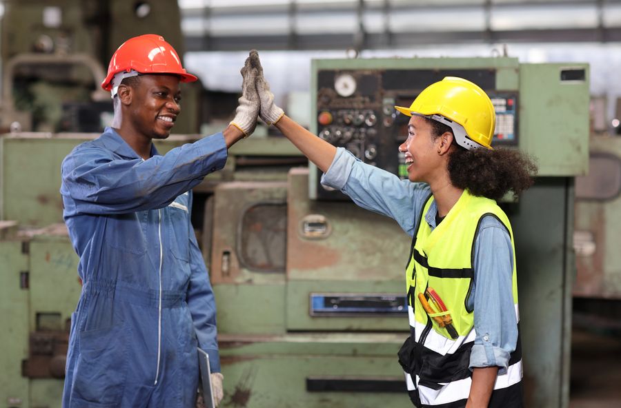 Two young workers in hard hats and workshop clothing high-fiving on the shop floor.