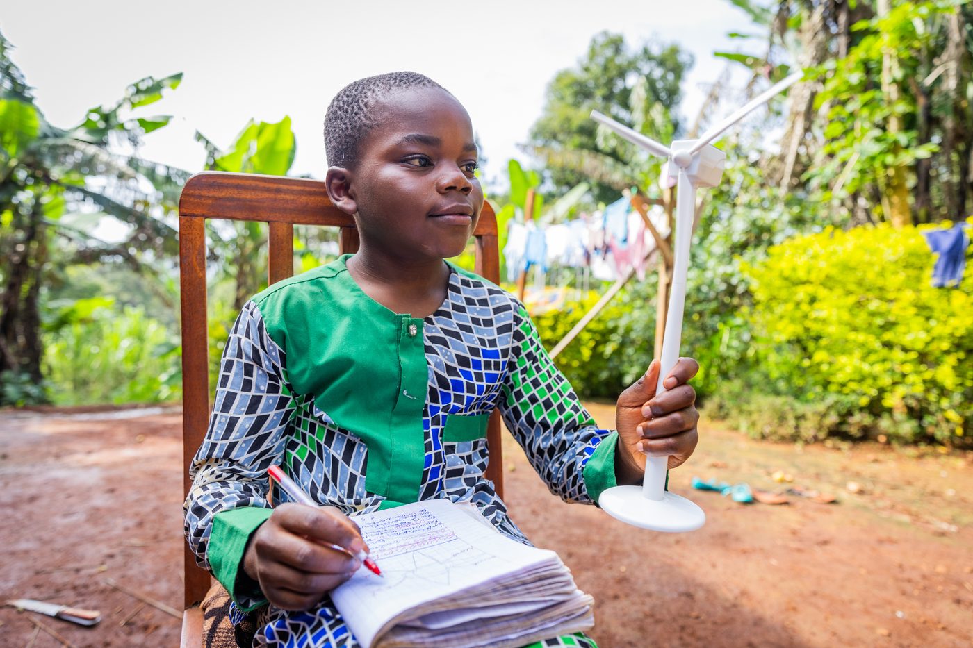 A boy holding a model wind turbine, notebook and pencil in hand
